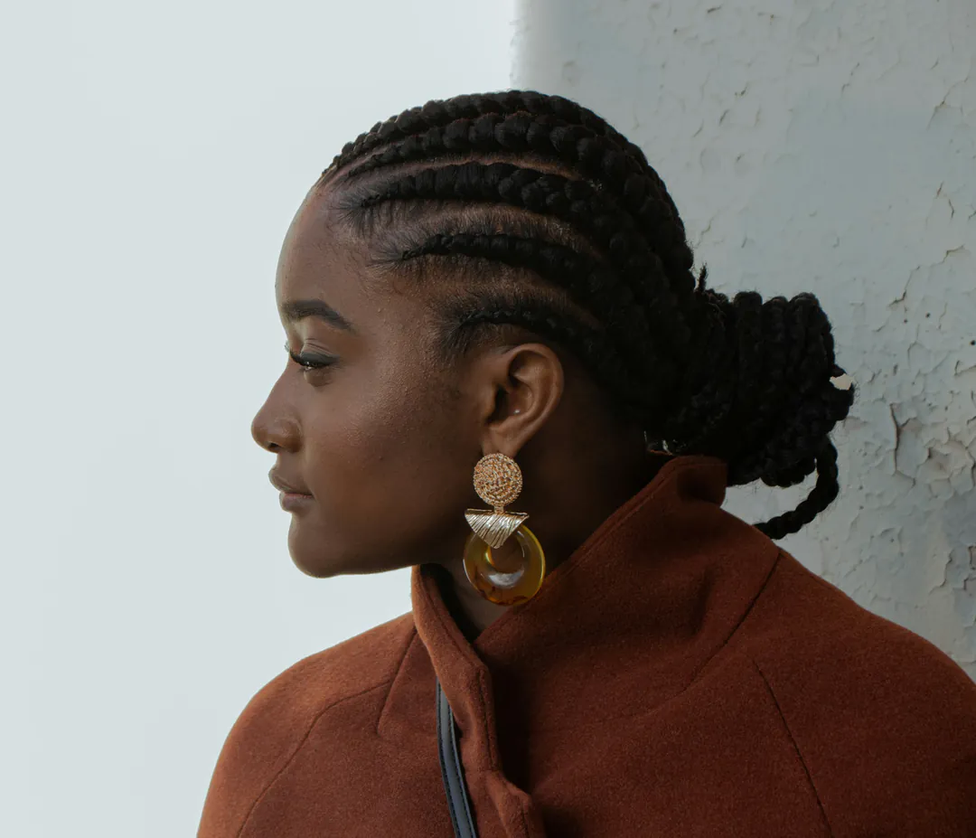 Model in profile wearing sculpted gold drop earrings against a grey backdrop